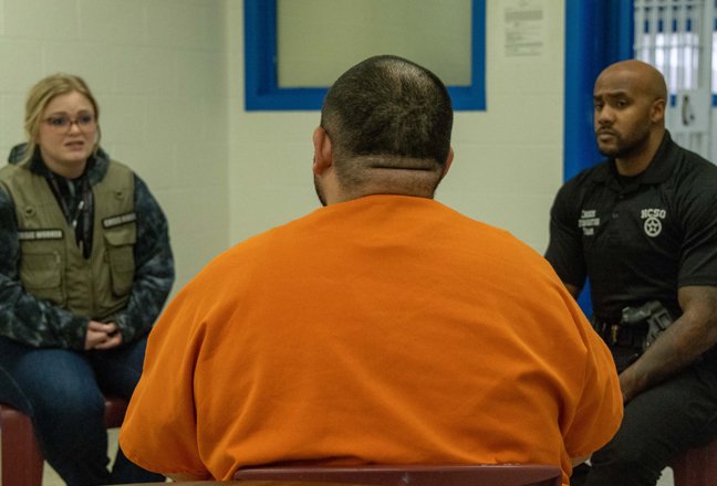 Two police officers talking to an inmate inside a jail cell